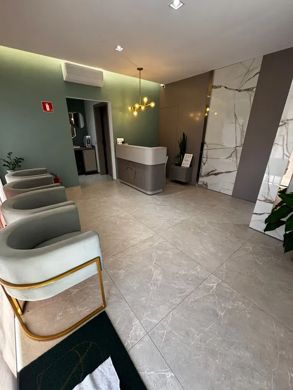 Recepção da clínica com poltronas verde-claro, detalhes dourados e piso de mármore